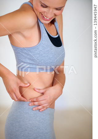 Fitness, stomach and woman holding skin for health, wellness and weight loss goals in a training studio. Smile, happy and young female person athlete showing body for exercise or workout at gym. Fitness, stomach and woman holding skin for health, wellness and weight loss goals in a training studio. Smile, happy and young female person athlete showing body for exercise or workout at gym. 139445947