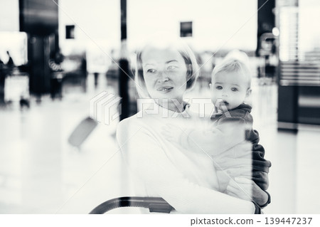 Thoughtful young mother looking trough window holding his infant baby boy child while waiting to board an airplane at airport terminal departure gates. Travel with baby concept Thoughtful young mother looking trough window holding his infant baby boy child while waiting to board an airplane at airport terminal departure gates. Travel with baby concept 139447237