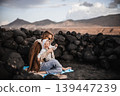 Mother enjoying winter vacations playing with his infant baby boy son on black sandy volcanic beach of Janubio on Lanzarote island, Spain on windy overcast day. Family travel vacations concept 139447239