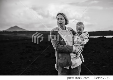 Mother enjoying winter vacations playing with his infant baby boy son on black sandy volcanic beach of Janubio on Lanzarote island, Spain on windy overcast day. Family travel vacations concept Mother enjoying winter vacations playing with his infant baby boy son on black sandy volcanic beach of Janubio on Lanzarote island, Spain on windy overcast day. Family travel vacations concept 139447240