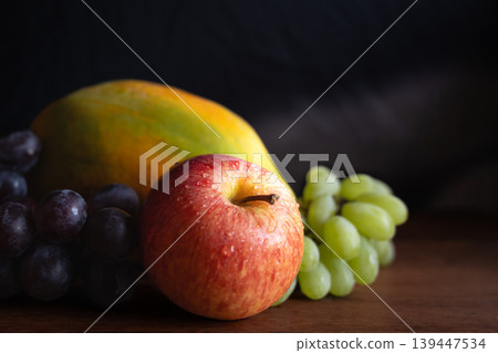 Apple grapes, papaya on the plate. Fresh organic fruits combination on dark background Apple grapes, papaya on the plate. Fresh organic fruits combination on dark background 139447534