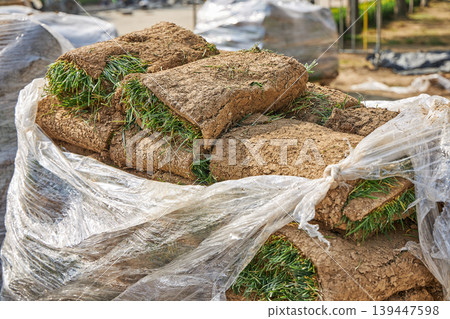 Stack of grass sod rolls wrapped in plastic film for park landscaping. Natural lawn turf prepared for installation. Professional garden renovation and soil improvement project. Stack of grass sod rolls wrapped in plastic film for park landscaping. Natural lawn turf prepared for installation. Professional garden renovation and soil improvement project. 139447598