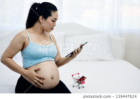 Pregnant woman using smartphone for online shopping while touching baby bump at home, digital maternity lifestyle and ecommerce payment concept for modern motherhood and prenatal preparation Pregnant woman using smartphone for online shopping while touching baby bump at home, digital maternity lifestyle and ecommerce payment concept for modern motherhood and prenatal preparation 139447624
