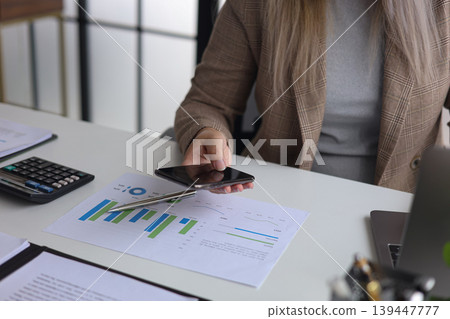 Businesswoman Analyzing Financial Data and Using Smartphone in Modern Office. 139447777