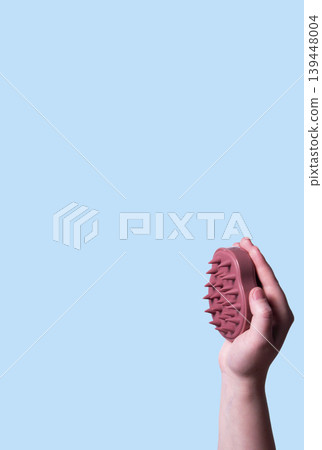 Pink scalp massager brush for hair treatment and care in human hand on blue background. Vertical Pink scalp massager brush for hair treatment and care in human hand on blue background. Vertical 139448004