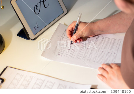 Physical over Digital concept. Woman training calligraphy at desk. Handwriting improves concentration and conceptual understanding better than digital notes. Perfect tool for mental clarity. Focus Physical over Digital concept. Woman training calligraphy at desk. Handwriting improves concentration and conceptual understanding better than digital notes. Perfect tool for mental clarity. Focus 139448190