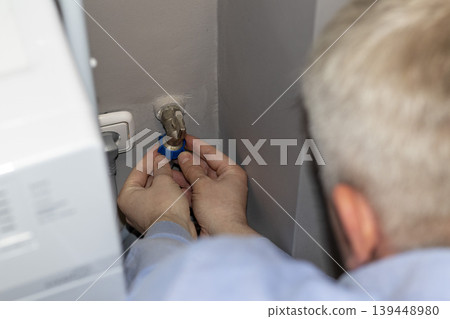 A worker installing or repairing a plumbing valve, likely for a washing machine A worker installing or repairing a plumbing valve, likely for a washing machine 139448980