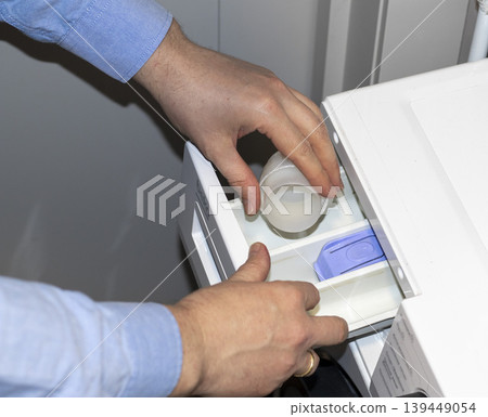Man opening the detergent dispenser drawer of a front-load washing machine, likely for servicing 139449054