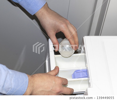 Man opening the detergent dispenser drawer of a front-load washing machine, likely for servicing 139449055