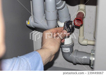 Plumber working on the plumbing drain pipes under a sink Plumber working on the plumbing drain pipes under a sink 139449067