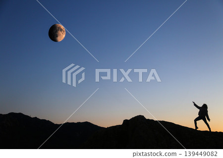 Silhouette of Woman Reaching Toward Moon in Mountain Landscape at Sunset Silhouette of Woman Reaching Toward Moon in Mountain Landscape at Sunset 139449082