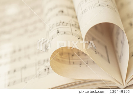 Music sheet pages curled into heart shape with notes, staff lines, paper folds, blurred score background. Concept of love music, romance, creativity, design, invitation, copy space Music sheet pages curled into heart shape with notes, staff lines, paper folds, blurred score background. Concept of love music, romance, creativity, design, invitation, copy space 139449195