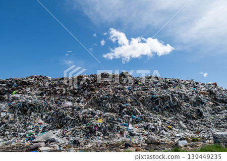 Large mound of trash at city landfill is visible under a clear blue sky with some clouds. Waste includes various types of refuse and debris Large mound of trash at city landfill is visible under a clear blue sky with some clouds. Waste includes various types of refuse and debris 139449235