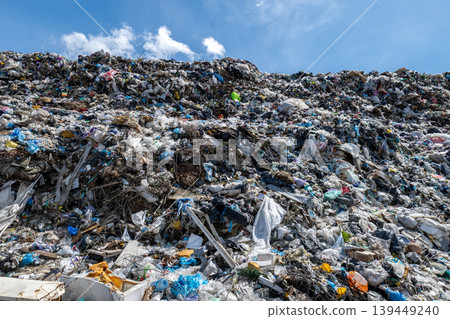 Large garbage landfill is seen with piles of trash and waste under a blue sky. Items include plastic, paper, and organic materials 139449240