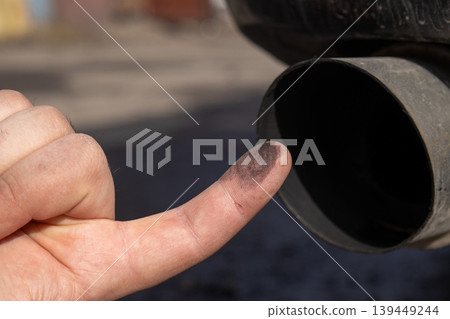 Mechanic inspects the exhaust pipe of a car. He checks for dirt and signs of wear. This occurs in a garage during daylight hours Mechanic inspects the exhaust pipe of a car. He checks for dirt and signs of wear. This occurs in a garage during daylight hours 139449244