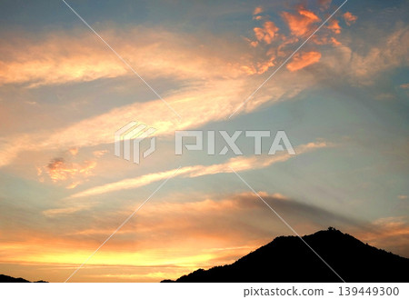 A fantastical evening sky scene, woven from crimson sunset clouds and mountain silhouettes. 139449300