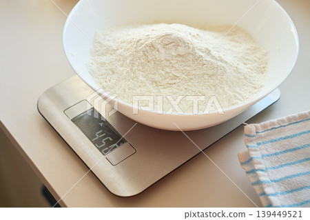 Bowl with flour sits on digital kitchen scale beside towel 139449521