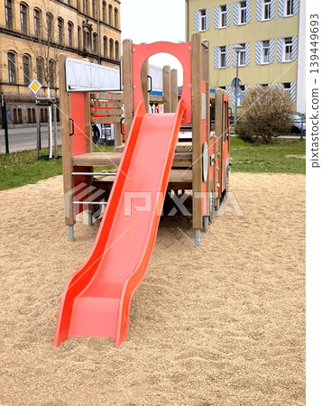 A bright red plastic slide on an empty playground in the city 139449693