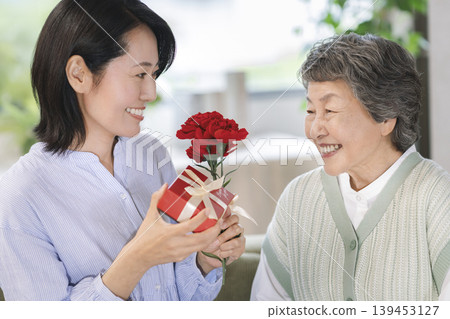 Mother's Day image: A middle-aged daughter gives a gift to her elderly mother. 139453127