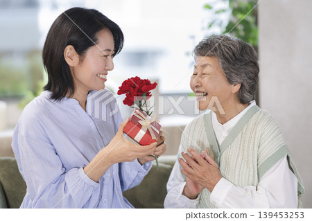 Mother's Day image: A middle-aged daughter gives a gift to her elderly mother. 139453253