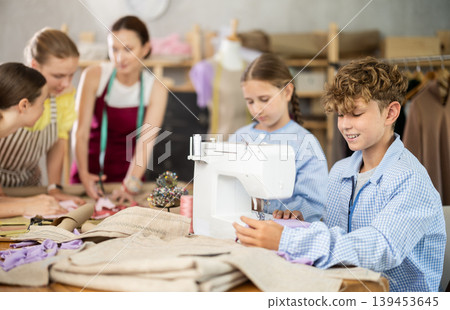 Tween boy stitching at machine during sewing class for children Tween boy stitching at machine during sewing class for children 139453645
