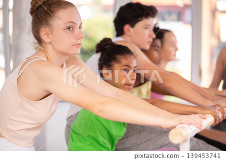 Teenage girl doing leg stretching exercise holding by ballet barre during dance courses 139453741