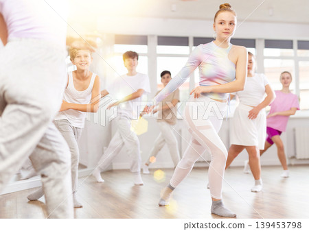 Female girl student repeats movements of unrecognizable teacher during group modern dance class. Female girl student repeats movements of unrecognizable teacher during group modern dance class. 139453798