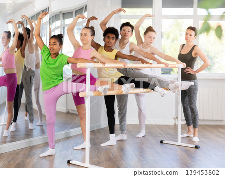 Dark-skinned teenage girl stretching at barre during beginner ballet class Dark-skinned teenage girl stretching at barre during beginner ballet class 139453802