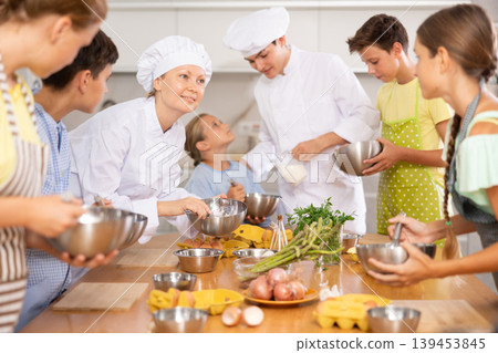 Young guy and adult woman cook teaches group of children to cook Young guy and adult woman cook teaches group of children to cook 139453845