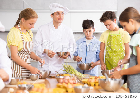 Friendly young chef running culinary courses for group of children Friendly young chef running culinary courses for group of children 139453850