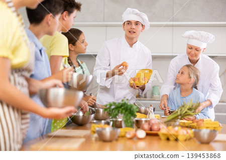 During cooking lesson, male cook tells children about culinary rules, woman assistant helps child 139453868
