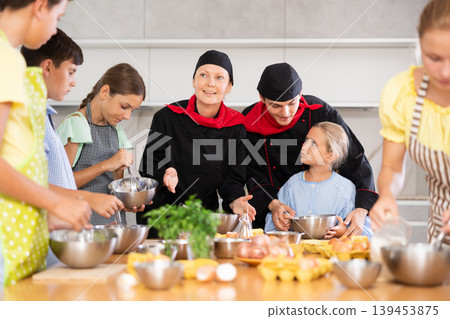 Young guy and adult woman cook teaches group of children to cook Young guy and adult woman cook teaches group of children to cook 139453875