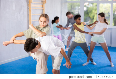 Girls and boys learns to do power grip with trainer during a self-defense lesson in gym Girls and boys learns to do power grip with trainer during a self-defense lesson in gym 139453902