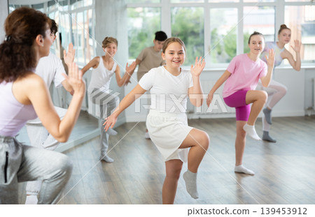 Female teacher performs choreographic exercises and teaches energetic mobile house dance together with teenagers Female teacher performs choreographic exercises and teaches energetic mobile house dance together with teenagers 139453912