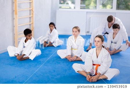 Tweens performing butterfly stretch during martial arts workout Tweens performing butterfly stretch during martial arts workout 139453919
