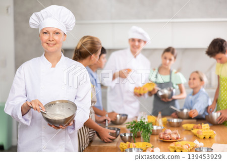 Smiling female chef sharing professional secrets during cooking masterclass for children 139453929