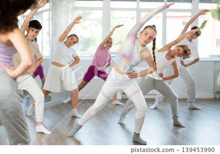 Female girl student repeats movements of unrecognizable teacher during group modern dance class. Female girl student repeats movements of unrecognizable teacher during group modern dance class. 139453990