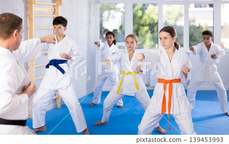 Children of different nationalities in kimono standing in fight stance during group karate training in gym 139453993