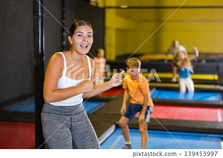 Teacher with children in trampoline center against background of children playing and jumping on trampoline Teacher with children in trampoline center against background of children playing and jumping on trampoline 139453997