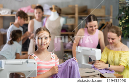 Teenage girl happily shows off a t-shirt he sewed with his own hands on sewing machine Teenage girl happily shows off a t-shirt he sewed with his own hands on sewing machine 139453998