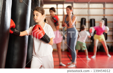 Teen girl in boxing gloves hits punching bag in gym Teen girl in boxing gloves hits punching bag in gym 139454012