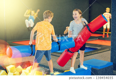 Children having funny wrestling by inflatable logs in indoor amusement park 139454035