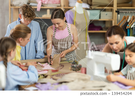 Teenage girl tries to sew on sewing machine. Teacher helps. Children watch and learn Teenage girl tries to sew on sewing machine. Teacher helps. Children watch and learn 139454204