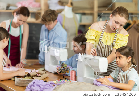Sewing lesson - a group of teenage children learn to sew on sewing machine and cut fabric Sewing lesson - a group of teenage children learn to sew on sewing machine and cut fabric 139454209