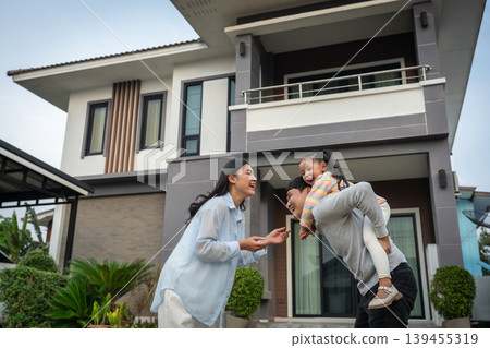 happy family, cheerful child girl piggy back on fatherwith mother while standing in front of their house happy family, cheerful child girl piggy back on fatherwith mother while standing in front of their house 139455319