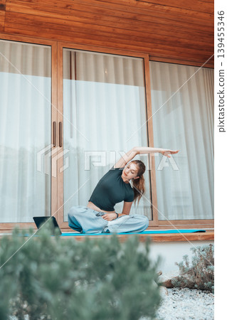 Young woman stretching on a terrace at home while following an online yoga session on a tablet Young woman stretching on a terrace at home while following an online yoga session on a tablet 139455346