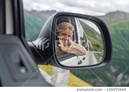 Young woman reflected in a car side mirror on an Alpine road trip, embracing freedom and travel Young woman reflected in a car side mirror on an Alpine road trip, embracing freedom and travel 139455644