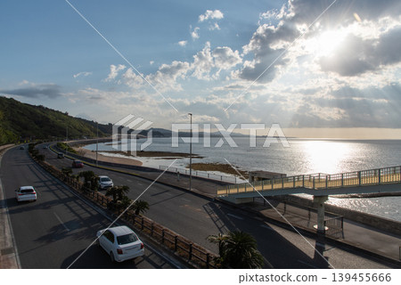 一座人行天橋橫跨海岸公路，陽光透過海面上的雲層縫隙從四面八方傾瀉而下。 139455666