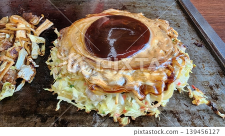 Japanese Okonomiyaki Savory Pancake with Special Sauce and Cabbage on a Hot Griddle Japanese Okonomiyaki Savory Pancake with Special Sauce and Cabbage on a Hot Griddle 139456127