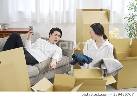 A man slacking off during a move while a woman packs her belongings. 139456707